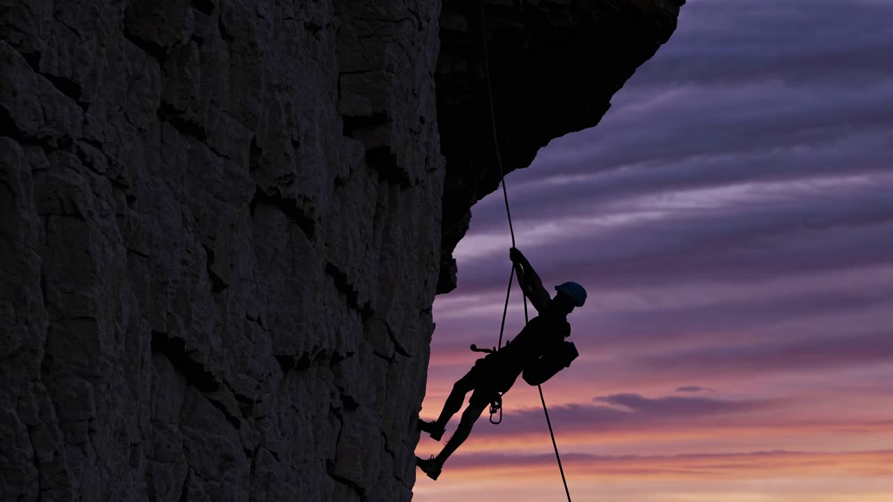 해가 지는 동안 바위 표면 을 내려가는 등반자 의 실루