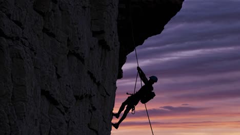 silueta de un escalador bajando en rappel por una pared rocosa al atardecer
