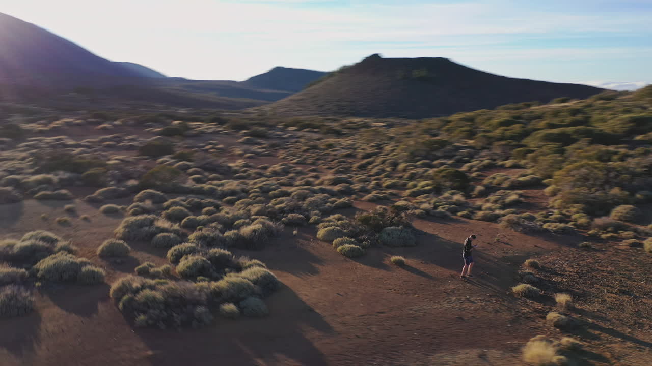 un tipo tomando una foto de sí mismo con un dron, caminando entre arbustos en una llanura debajo del teide, españa