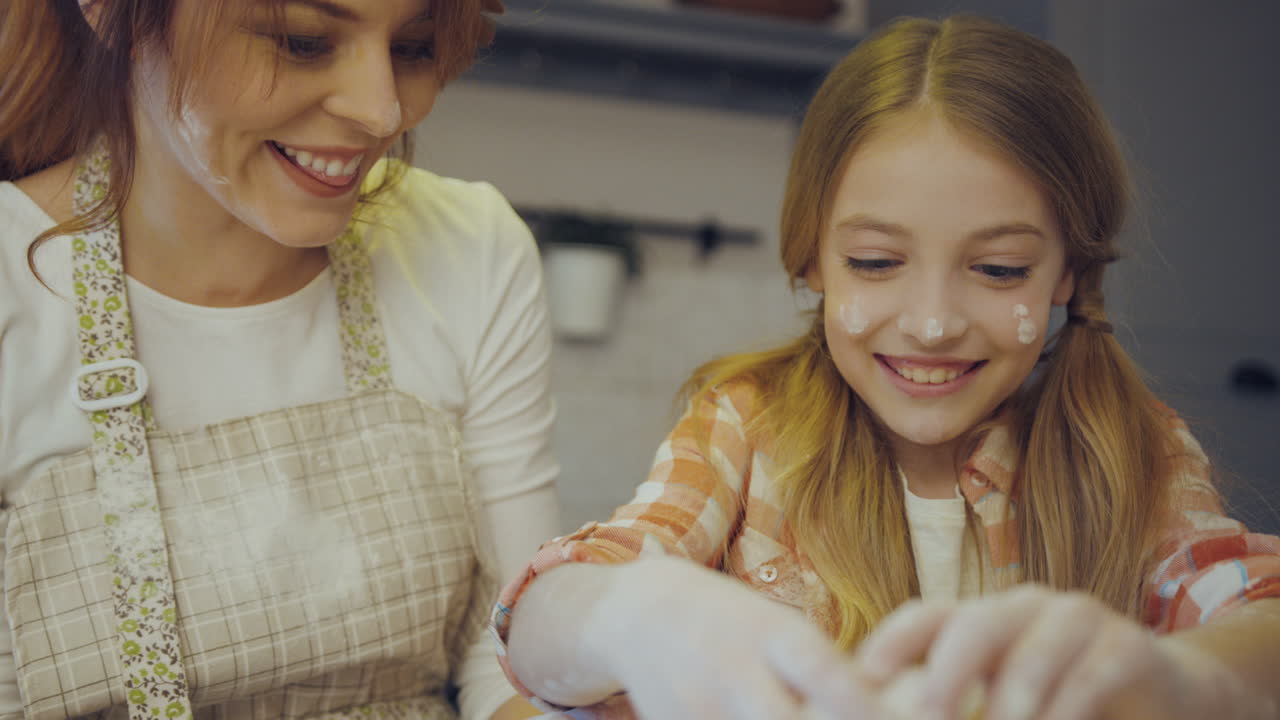Close up of the mother's and daughter's hands breaking an egg to the glass bowl with a daugh inside. Portrait shot in the kitchen while cooking.
