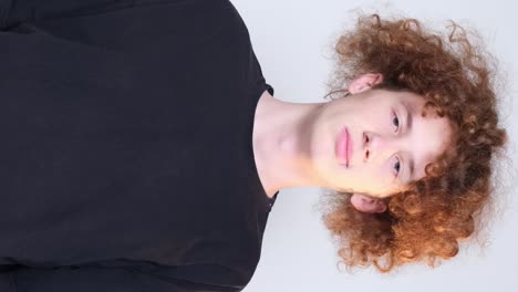 Portrait of a Young Curly Guy in a Black Tshirt on a Light Blue Background Looking at the Camera Portrait of a Young Curly Guy in a Black Tshirt on a Light Blue Background Looking at the Camera the Young Man Spreads his Hands Emotions Facial Expressions and Gestures on Camera