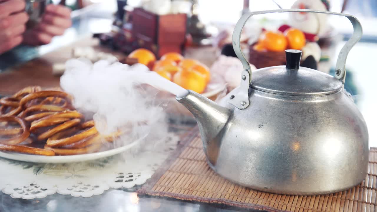Hot water with white smoke is pouring from the kettle into cup. Santa's hand hold hot kettle on the table background