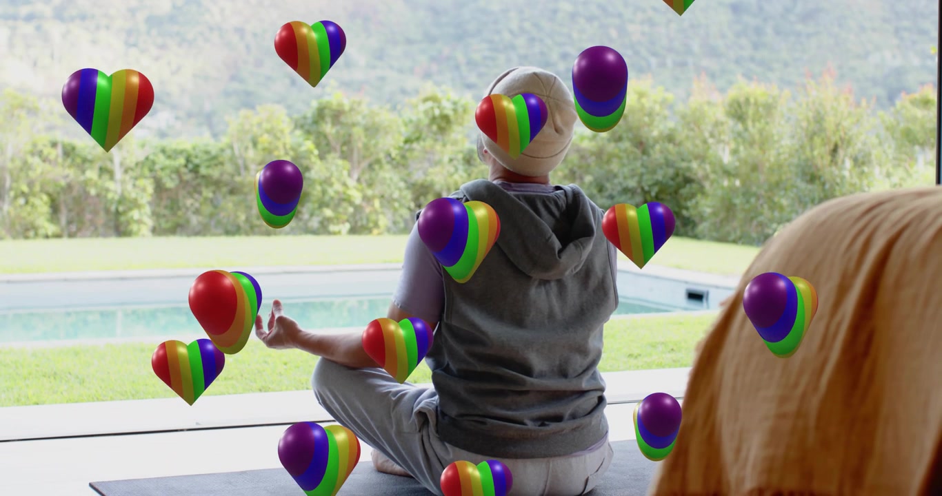 Man beoefent yoga op het terras bij het zwembad en verwelkomt drijvende regenbooghartballonnen door de handpalmen te heffen.
