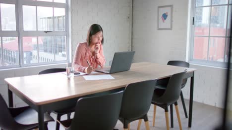 Focused-asian-businesswoman-using-laptop-and-taking-notes,-at-table-in-meeting-room,-in-slow-motion