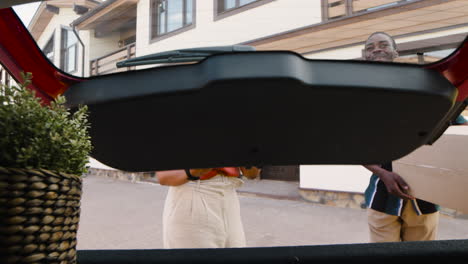 woman opening car trunk while her son, ready to moving home, putting a carton box inside and then they embracing each other to say goodbye