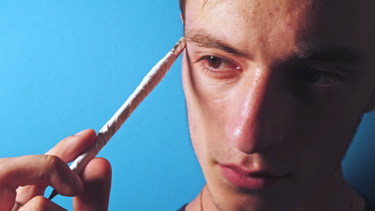 Close-up slow motion of thinking man with a pencil in front of a blue background