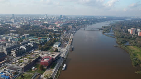 Forwards-fly-above-Vistula-river-calmly-flowing-through-town.-Modern-building-of-Copernicus-Science-Centre-with-planetarium-on-riverbank.-Aerial-panoramic-view.-Warsaw,-Poland