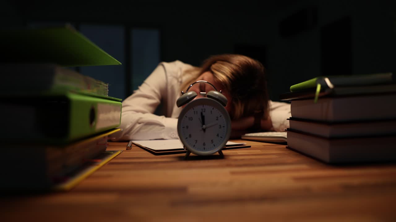 Persona esausta che dorme sulla scrivania con una sveglia