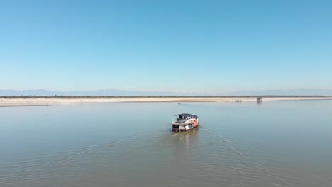 4K-Drohnenaufnahme-Einer-Yacht,-Die-Einen-Fluss-Hinuntersegelt,-Mit-Wunderschönen-Bergen-Im-Hintergrund