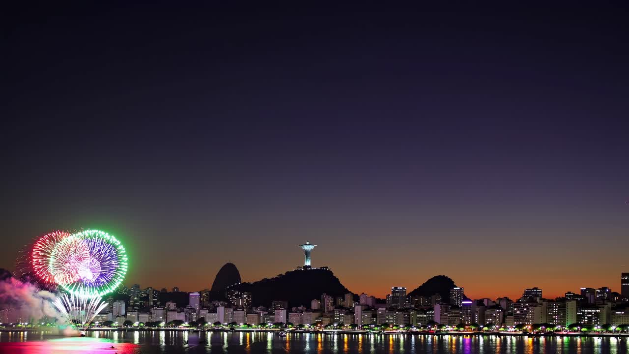 A wide-angle video captures a vibrant city skyline at dusk, with fireworks illuminating the sky