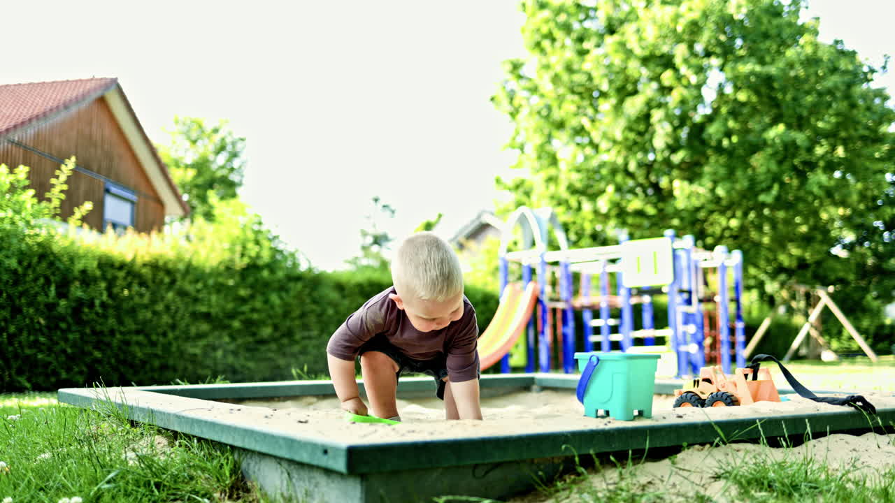 Toddler boy in t-shirt and shorts playing in sandbox in summer. Child on playground playing with sand. Toddler digging sand outdoors. Child development and environmental exploration