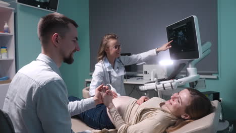 pregnant woman having ultrasound scan at the gynecologist office while loving husband holding her hand 10