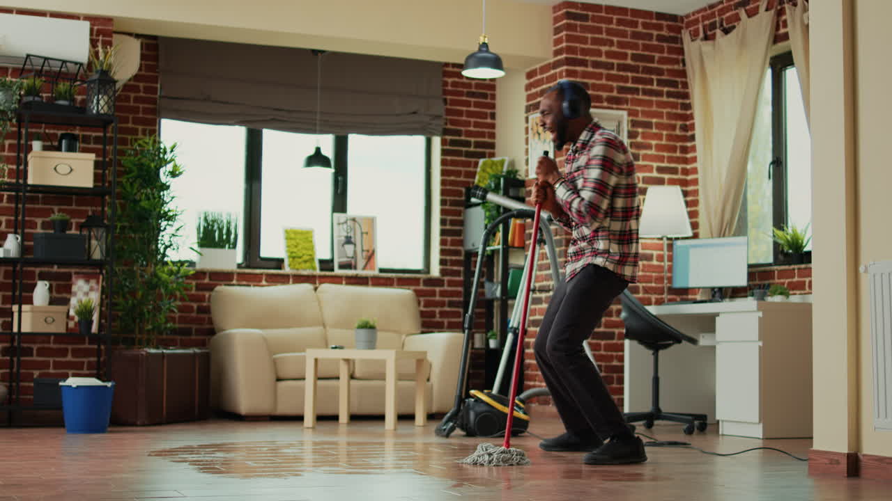 Young male adult having fun with mop and music at home