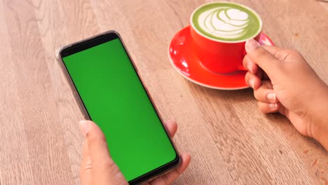 mujer usando un teléfono de pantalla verde mientras bebe matcha latte