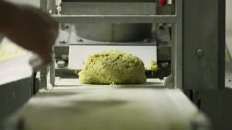 Brotbacken-In-Der-Bäckerei---Hand-Des-Bäckers,-Der-Den-Rohen,-Gelben,-Abgerundeten-Teig-Aus-Der-Teigrollanlage-Nimmt---Nahaufnahme,-Zeitlupe