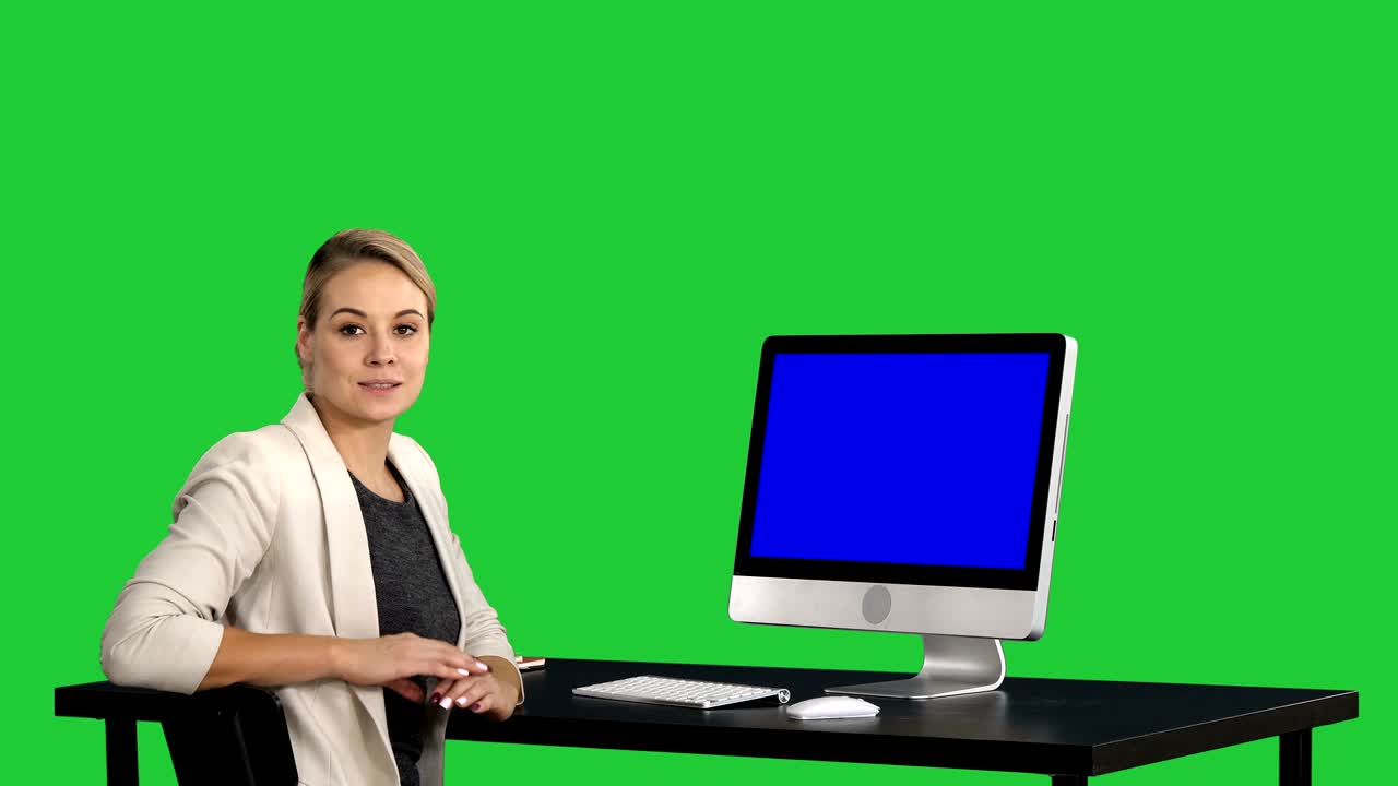 mujer de negocios confiada y enfocada hablando con la cámara y mirando para monitorear cerca de ella en una pantalla verde, clave de croma. pantalla azul muestra de maqueta