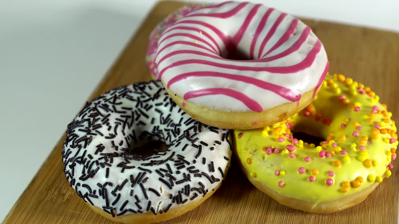 rosquillas giratorias con diferentes rellenos en la mesa. deliciosa rosquilla dulce girando en un plato. rosquilla brillante y colorida macro disparo de primer plano girando sobre un fondo blanco. bucle sin costuras.