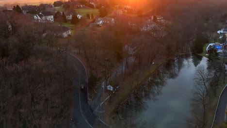 Jeep-car-driving-up-twisting-road-beside-picturesque-lake-in-winter-with-golden-sunlight-from-sunset