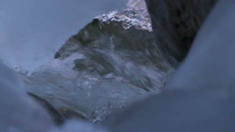 cold water of mountain creek flowing under glacier and ice at winter, frozen snow landscape