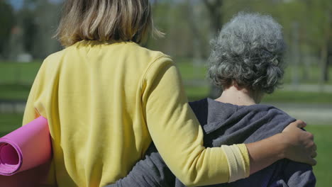 women embracing each other, holding yoga mat in hands, laughing