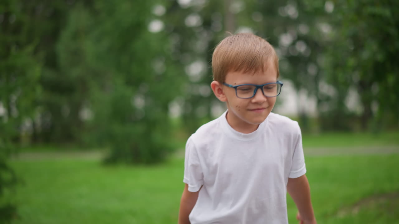 A young boy with glasses happily runs forward, but his expression changes to one of seriousness as he approaches his bicycle, wearing a white shirt and denim shorts