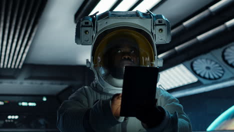vertical video astronaut wearing spacesuit monitoring mission data on tablet in spacecraft