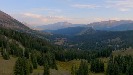 Slow-pull-back-over-mountain-valley-an-trees-with-mountain-range-on-the-horizon-in-Crested-Butte,-Colorado-on-a-beautiful-day