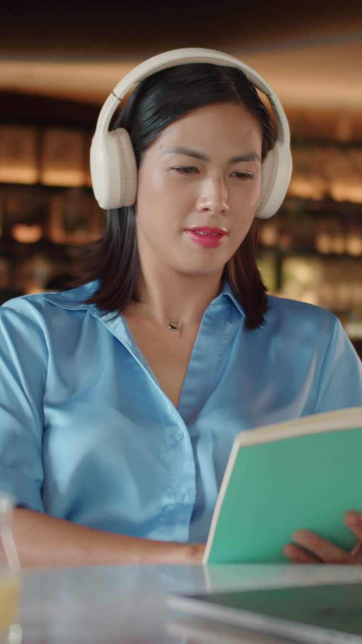 Asian Woman Listening to Music and Reading Book in Cafe