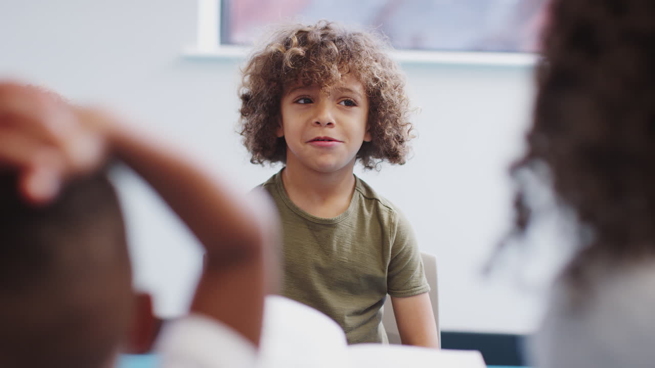 Young mixed race schoolboy sitting with classmates at infant school making faces, selective focus
