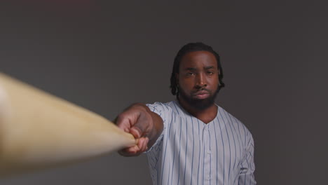 retrato de estudio de un jugador de béisbol masculino serio con la camiseta del equipo sosteniendo el bate hacia la cámara disparado contra un fondo gris