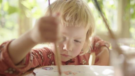 a cute kid with a bruised and cut eye makes art in a sunny room with plants