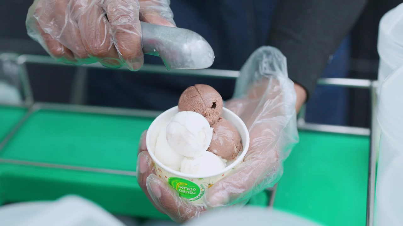 Close-up of vendor in plastic gloves scooping ice cream into a cup in Thailand.