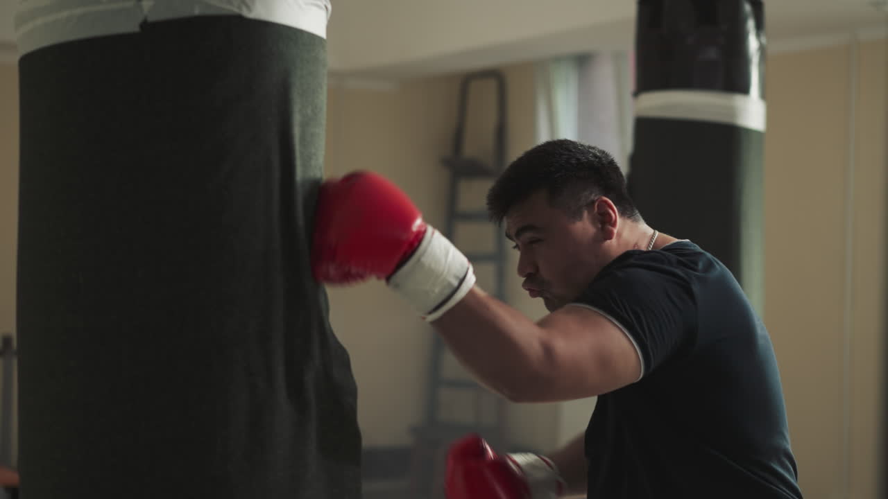 Athlete combats punching bag in sports club. Aggressive sportsman beats training equipment in empty gym slow motion. Martial arts development