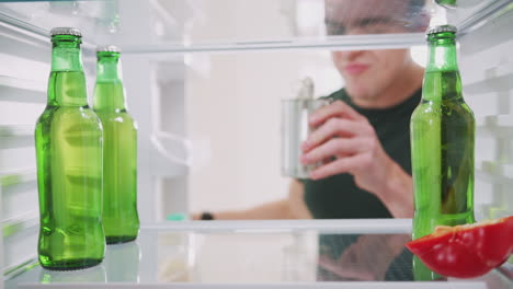 vista mirando dentro del refrigerador vacío excepto por la lata abierta y la botella de cerveza en el estante