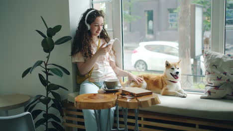 woman with headphones listening to music and petting her dog in a cafe