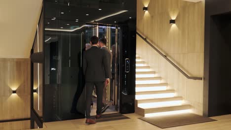 a group of business people enter a modern elevator and discussing corporate meeting in business center. international delegation of legal services experts take lift. the door closes. lighting stairs.