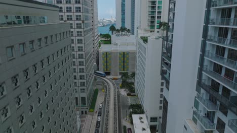 aerial ascending footage of rail car driving on tracks leading between high rise buildings. futuristic concept of passenger transport. miami, usa