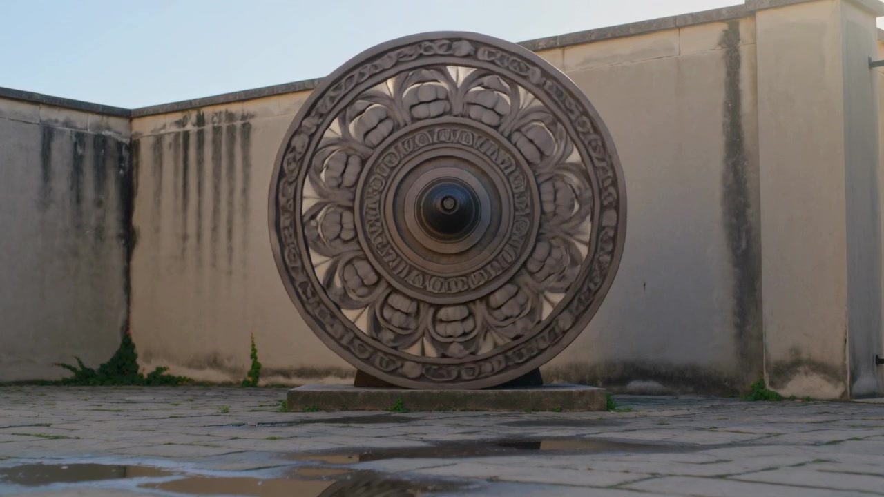 Registrazione di una ruota circolare ornata che ruota lentamente su un basso piedistallo in un cortile chiuso, con pozzanghere.