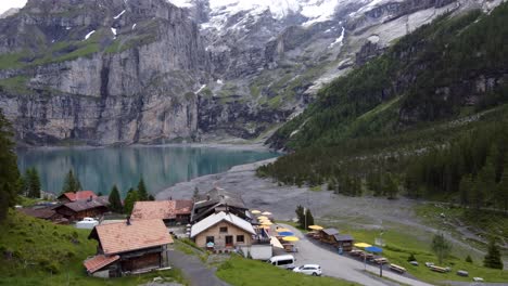 Drone-Aerial-:-young-hiker-sitting-on-a-rock-up-the-mountain-cafeteria-facing-view-to-Bluemlisalp-giant-mountains-surrounding-the-turquoise-szure-glacier-lake-Oeschinensee-in-Kandersteg,-Switzerland