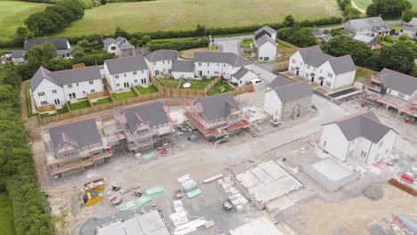 Drone-view-of-half-built-new-homes-development-in-a-rural-village-in-the-UK,-surrounded-by-greenery-and-fields