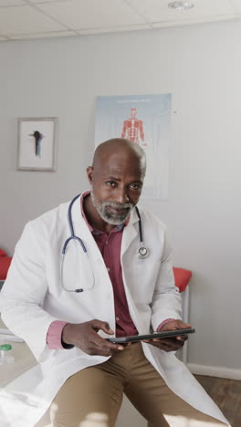 vertical video of portrait of african american male doctor using tablet, slow motion