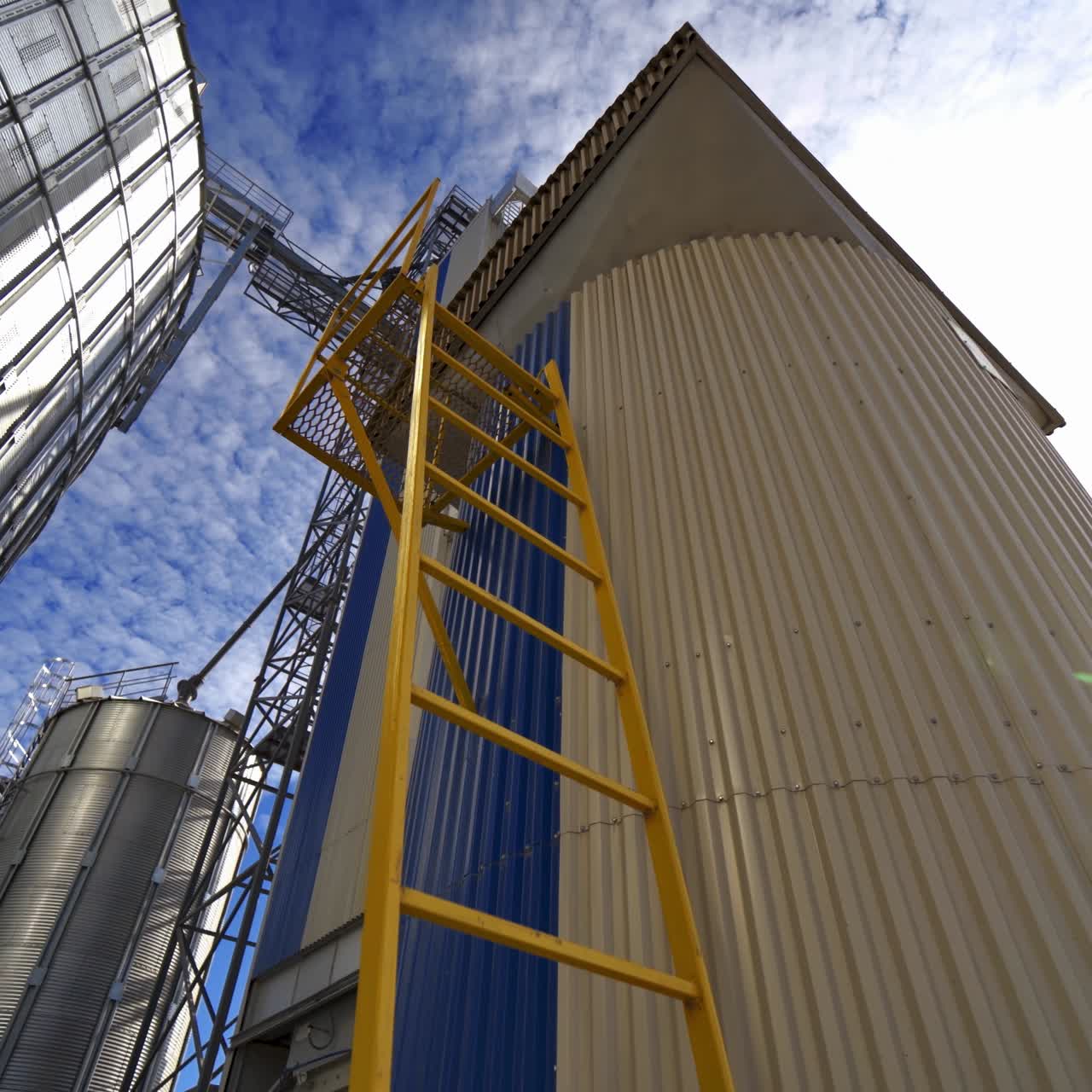 Modern large granary at sunlight. Agricultural manufacturing. Agriculture grain silos storage tank. Large metal silos on blue sky background.