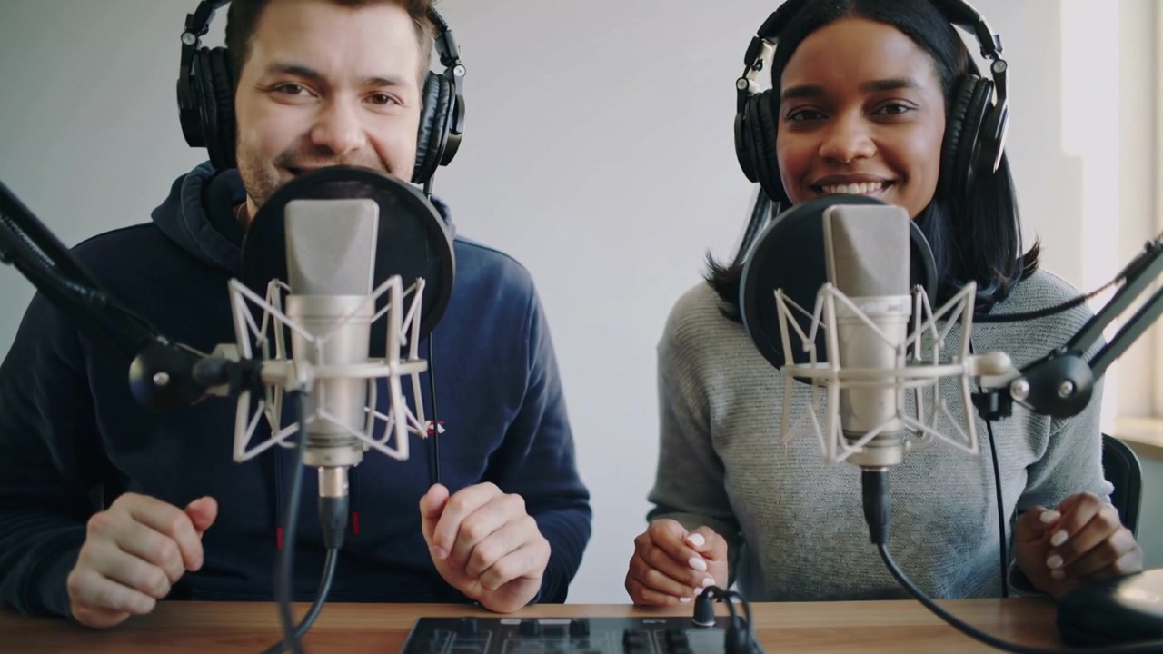 Lifting phones, hosts in hoodie and sweater adjusting tapping mixer preparing recording in studio
