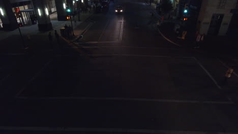 Aerial-drone-shot-of-car-standing-in-the-red-signal-in-the-city-with-people-crossing-the-road-at-night