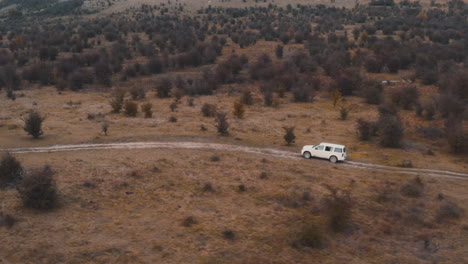 White-jeep-driving-on-a-country-road-in-a-brown-autumn-steppe,Czechia