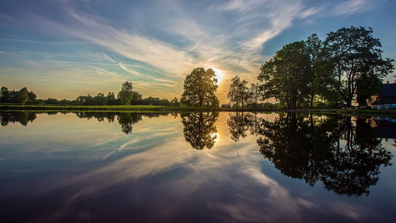 Timelapse shot of beautiful sunset over lake surrounded by trees with artistic clouds passing by
