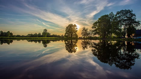 Timelapse-shot-of-beautiful-sunset-over-lake-surrounded-by-trees-with-artistic-clouds-passing-by