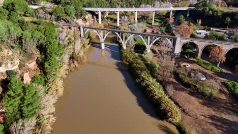 Aerial view of three bridges crossing a river in a green valley, showing modern and historical architecture surrounded by nature.