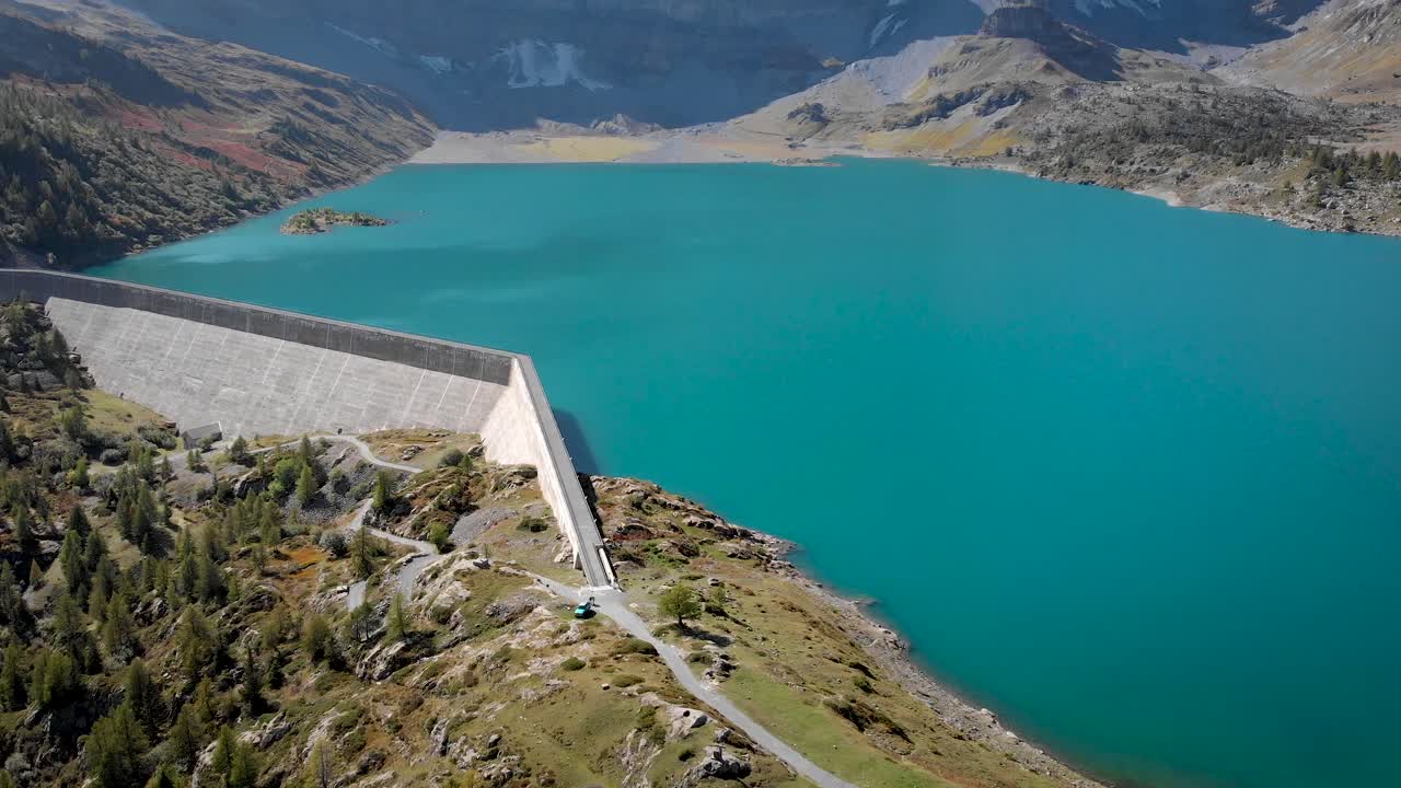 Aerial view of Lac de Salanfe and its hydroelectric dam in Valais, Switzerland on a sunny autumn day in the Swiss Alps with a pan up view from the turquoise waters up to alpine peaks and cliffs