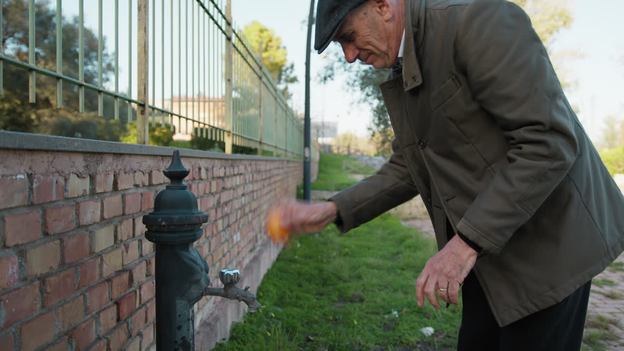 Man Washes a Tangerine at the Park Fountain Before Eating